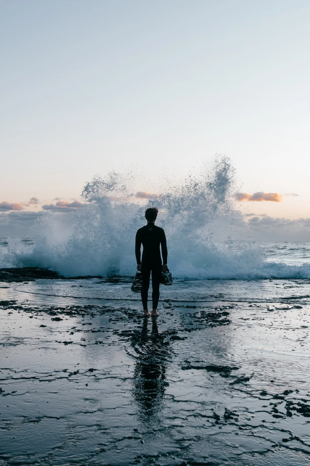 Gui standing on the rocks as a wave breaks behind him